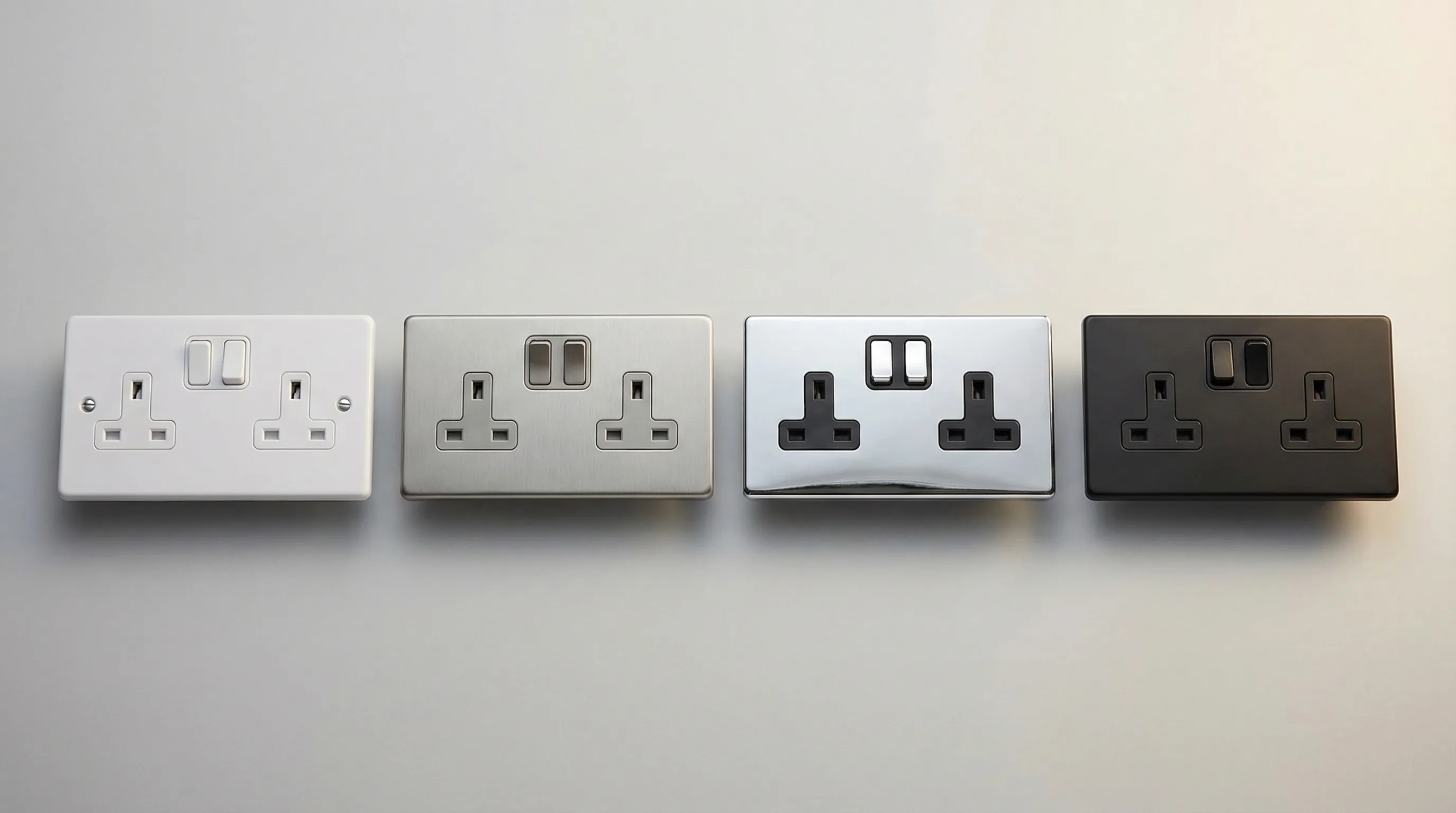 Double gang socket faceplates in white plastic, brushed chrome, and matt black finishes arranged side by side