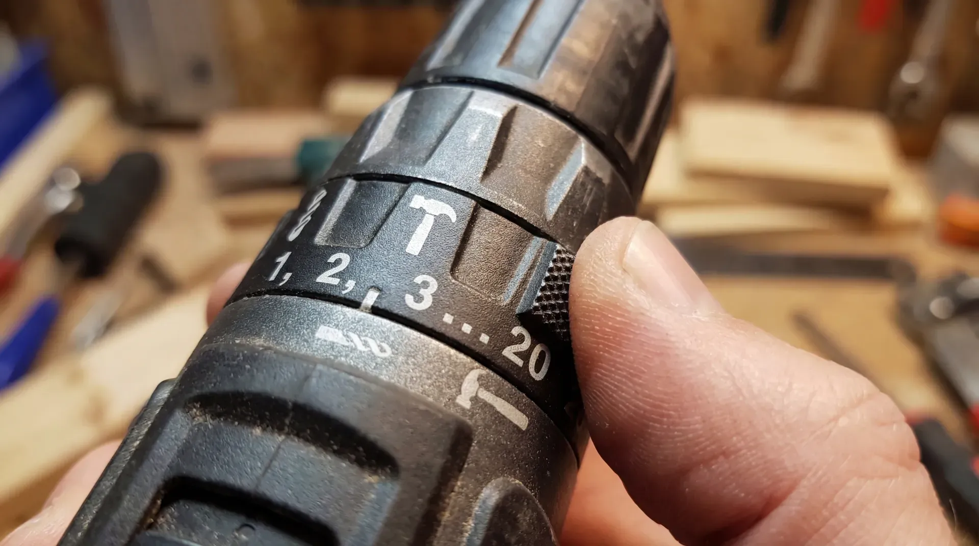 Close-up of a combi drill mode selector collar showing numbered torque settings from 1 to 20, a drill bit icon, and a hammer icon, with a finger turning the collar